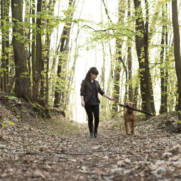 Frau geht mit Hund auf Waldweg spazieren