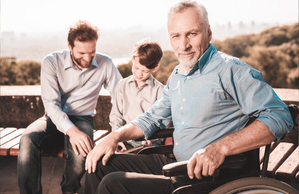 Mann im Rollstuhl mit Seinem Sohn und seinem Enkel im Hintergrund
